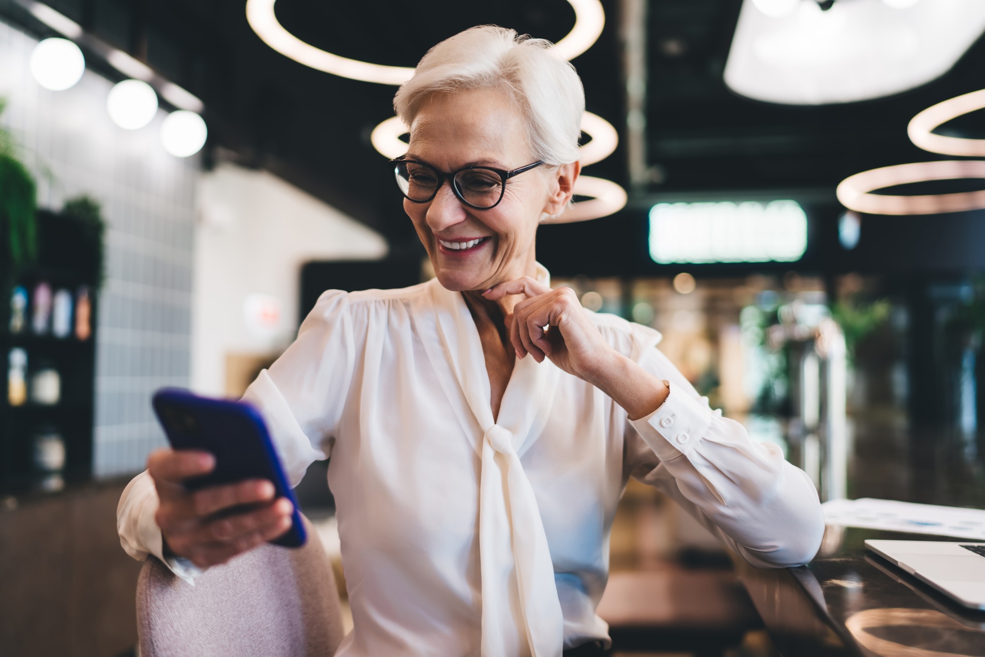 Cheerful senior woman sitting with smartphone